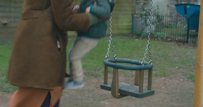Mother helping toddler into swing before pushing him