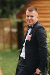 Portrait of young groom. Man stand outside in the garden. Wedding suit with tie-bow