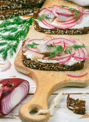 Open sandwich with salted fish herring  (mackerel), cottage cheese (ricotta), dill and pickled red onions on rye bread with seeds. Gourmet snack. Selective focus