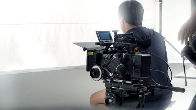 Behind video camera that recording online commercial or web film movie in the big studio production with professional equipment such as high resolution cam and monitors and LED light with crew team