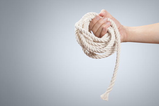 Male hand holding a roll of thin natural rope on grey background