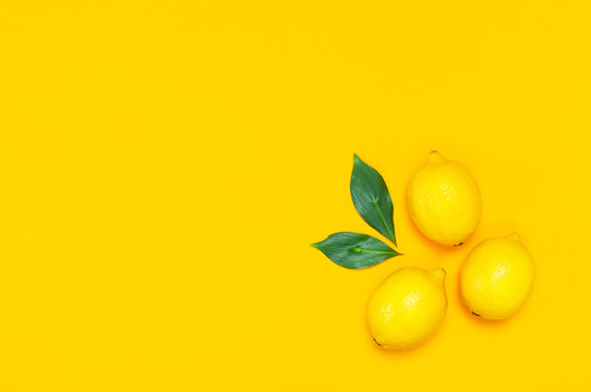 Ripe juicy lemons and green leaves on bright yellow background. Lemon fruit, citrus minimal concept, vitamin C. Creative summer food minimalistic background. Flat lay, top view, copy space.