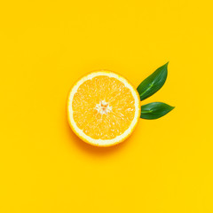 Ripe juicy orange and green leaves on bright yellow background. Orange fruit, citrus minimal concept, vitamin C. Creative summer food minimalistic background. Flat lay, top view, copy space.