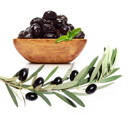 Black olives in wooden bowl with branch or twig  isolated on white background