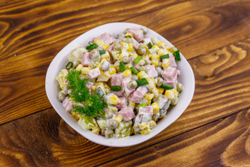 Tasty salad with sausage, green pea, canned corn, bell pepper, cucumber and mayonnaise on wooden table. Top view