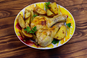 Baked chicken drumsticks with potatoes in a plate on wooden table