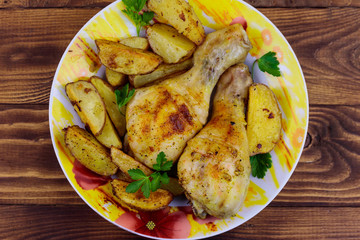 Baked chicken drumsticks with potatoes in a plate on wooden table