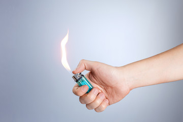 Hand burning a lighter on gray background - obrazy, fototapety, plakaty
