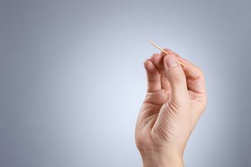 Hand holding toothpick on gray background