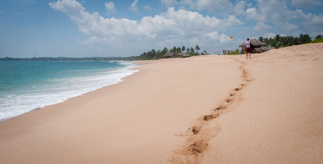 A man and a woman walk along a wide sandy beach along the ocean in Sri Lanka.