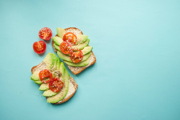 Flat lay of delicious toasts with sliced avocado, tomatoes and sesamum seeds on blue background with copyspace. Healthy food concept.