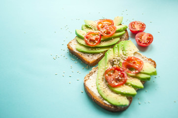 Flat lay of delicious toasts with sliced avocado, tomatoes and sesamum seeds on blue background with copyspace.