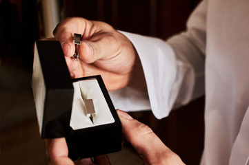 A man fastens with a cufflink on the cuff of the sleeve of a luxurious white shirt.