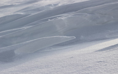 Abstract winter background of white snow drifts and dunes. Nature makes patterns and difficult textures on the clear snow surface