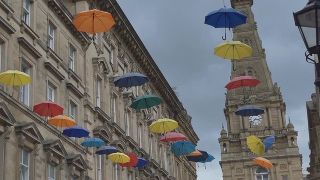 A panning shot of a street with many colourful umbrellas hanging on wires.