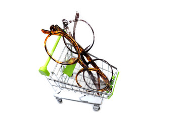 Frames of glasses are in a small shopping cart. Eyewear sales concept. Isolated