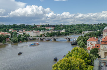Fototapeta premium View of Prague from the dancing house. One of the many bridges, the Vltava River and the ships on it. A lot of greenery, parks and forests, blue sky with clouds. A wonderful place to travel in Europe.