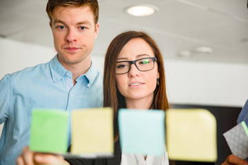 Businesswoman And Colleague Looking At Notes Stuck On Glass