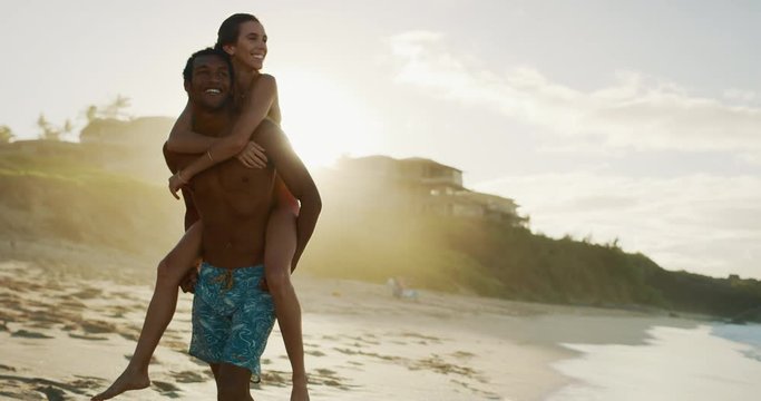 Happy couple playing on the beach at sunset, mixed race couple