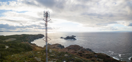 Obraz premium Aerial view of a communication tower on a rocky Atlantic Ocean Coast during a cloudy sunset. Taken in Twillingate, Newfoundland, Canada.