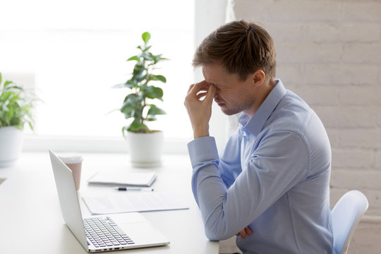 Tired businessman massaging nose bridge, feeling eyes strain, discomfort, exhausted man suffering from computer vision syndrome after long laptop use, eyesight relaxation, health problem