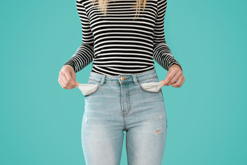 Young woman showing doesn't has nothing in her jeans pockets on blue background.