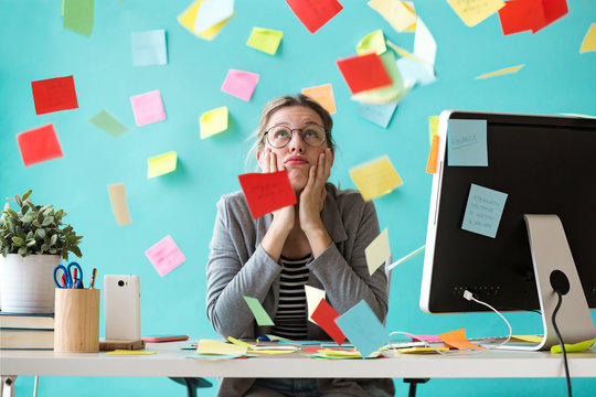 Stressed young business woman looking up surrounded by post-its in the office.
