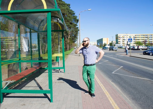 Bearded Man In Sunglasses At The Bus Stop Talking On The Phone