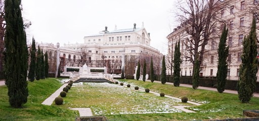 Obraz premium Winter park with a frozen fountain and sculptures in Vienna. In the distance you can see the Hofbroek building.