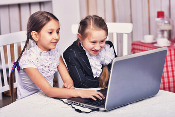 Two children girls look at a laptop, play, participate in chat, learn, communicate via the Internet
