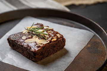 Homemade dark chocolate brownies topping with almond slices stacked on dark plate with copy space....