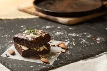 Homemade dark chocolate brownies topping with almond slices stacked on dark plate with copy space....