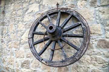 Old wooden wagon wheel leaning up against a stone wall