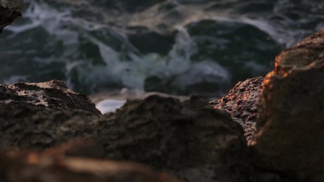 waves hit the rocks on the beach at sunset
