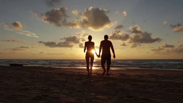silhouette of couple walking towards sea shore 