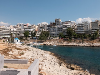 Rocky coastline of Agios Nikolaos Bay, Saronic gulf, Aegean sea, boats and Agios Nikolaos Chapel at...