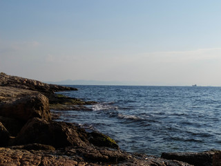Fototapeta na wymiar Rocky seashore, splashing waves and ships on the horizon. Piraeus, Greece