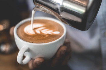 Barista pour milk into a cup of coffee. Coffee latte art in cafe. soft focus, blur, noise.
