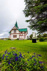 View from the park at wooden Church in Husavik town in Nordurting municipality on the North coast of Iceland. Blue flowers are at the foreground