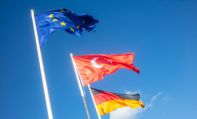 German, EU, Turkey waving flags on white poles. Blue sky background.