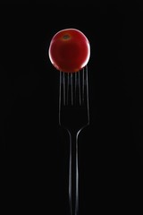 little red tomato on a fork on a black background