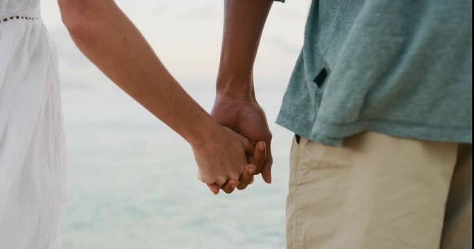 Beautiful couple holding hands on a tropical beach at sunset, mixed race