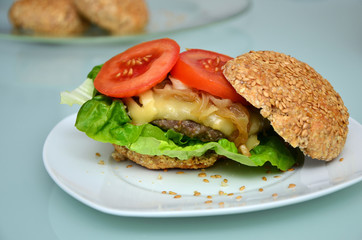 Gesundes Sandwichbrötchen mit Cheeseburger, gebratenen Zwiebeln und Tomatenscheiben