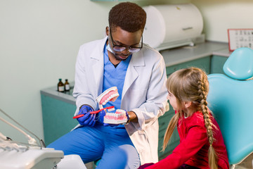 Young beautiful girl in dental office. African children's dentist examines teeth to a child.