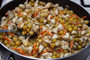 Chopped chicken in a pan with chopped carrots and peas