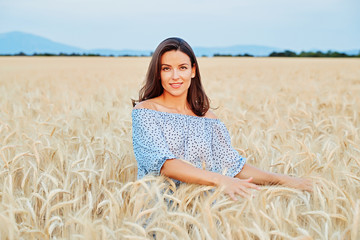 Fototapeta na wymiar The beautiful young girl with long brunette hairs poses in the field with wheat, sunset light, turns, smiles, flirts, happy, blue dress, France, Provence