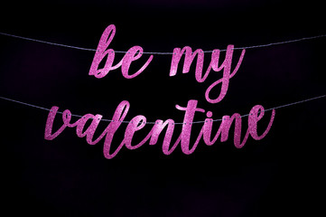 Be My Valentine message in sparkling handwritten pink script banner hanging across a dark black background