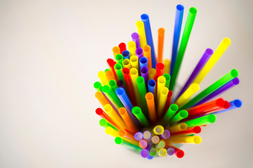 Glass full of brightly colored plastic straws sticking up next to neutral wood copy space