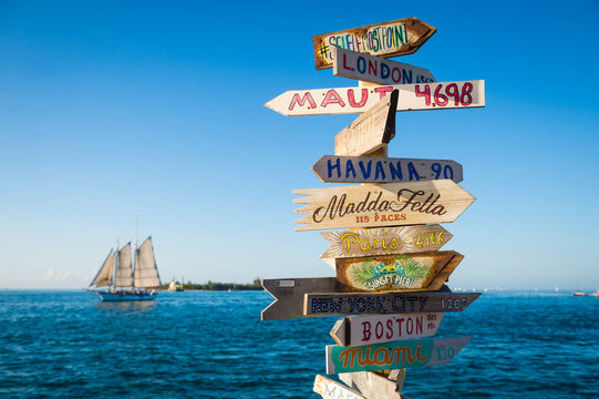 Bright scenic view of rustic wooden direction sign with sailboat in Key West, Florida, USA