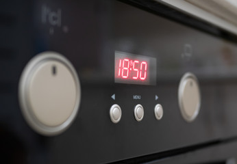 closeup of control buttons and time display of modern kitchen electrical oven. selective focus on red numbers of digital clock. control dials hidden